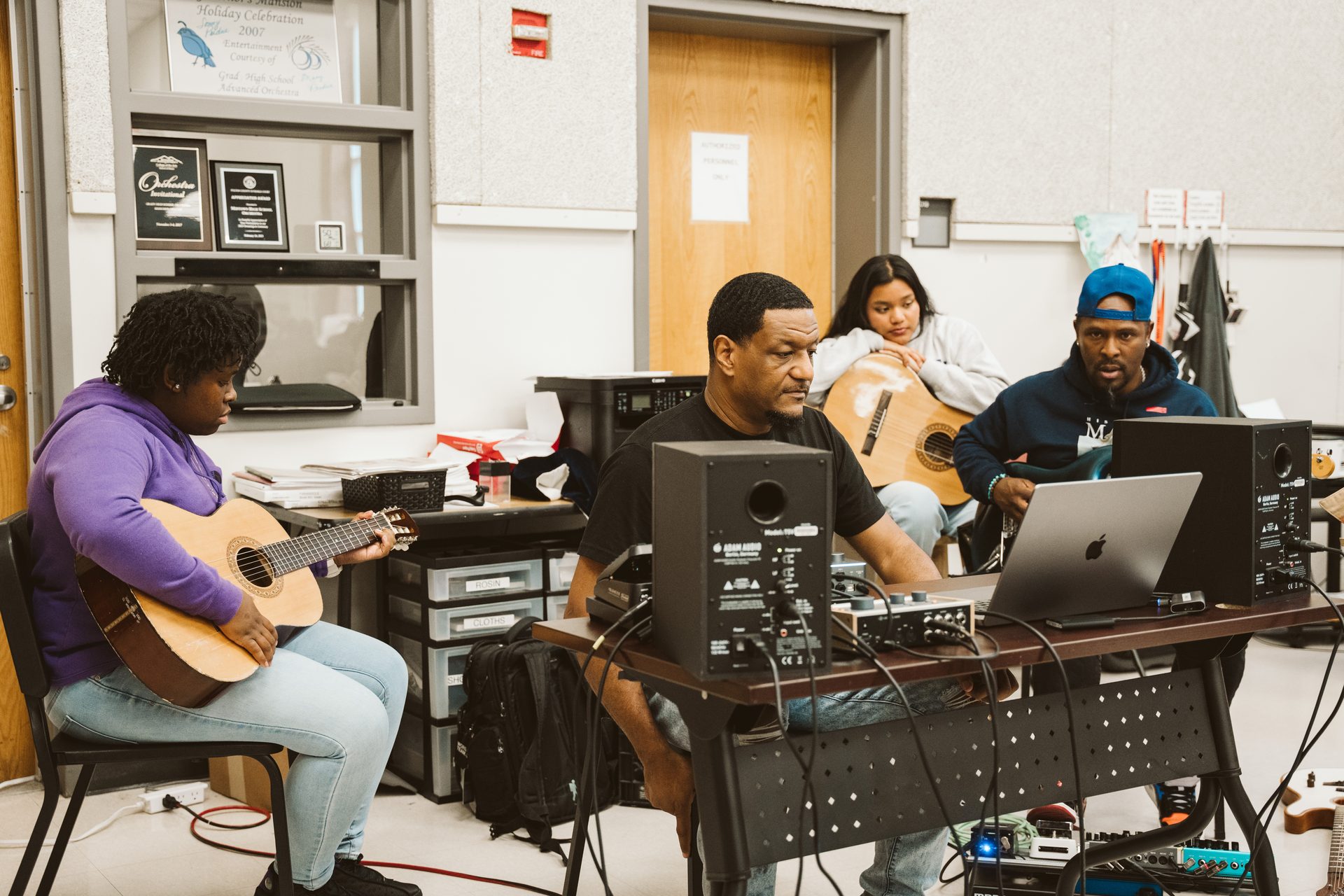 Keyz Bridgez at the production desk with students playing acoustic guitars